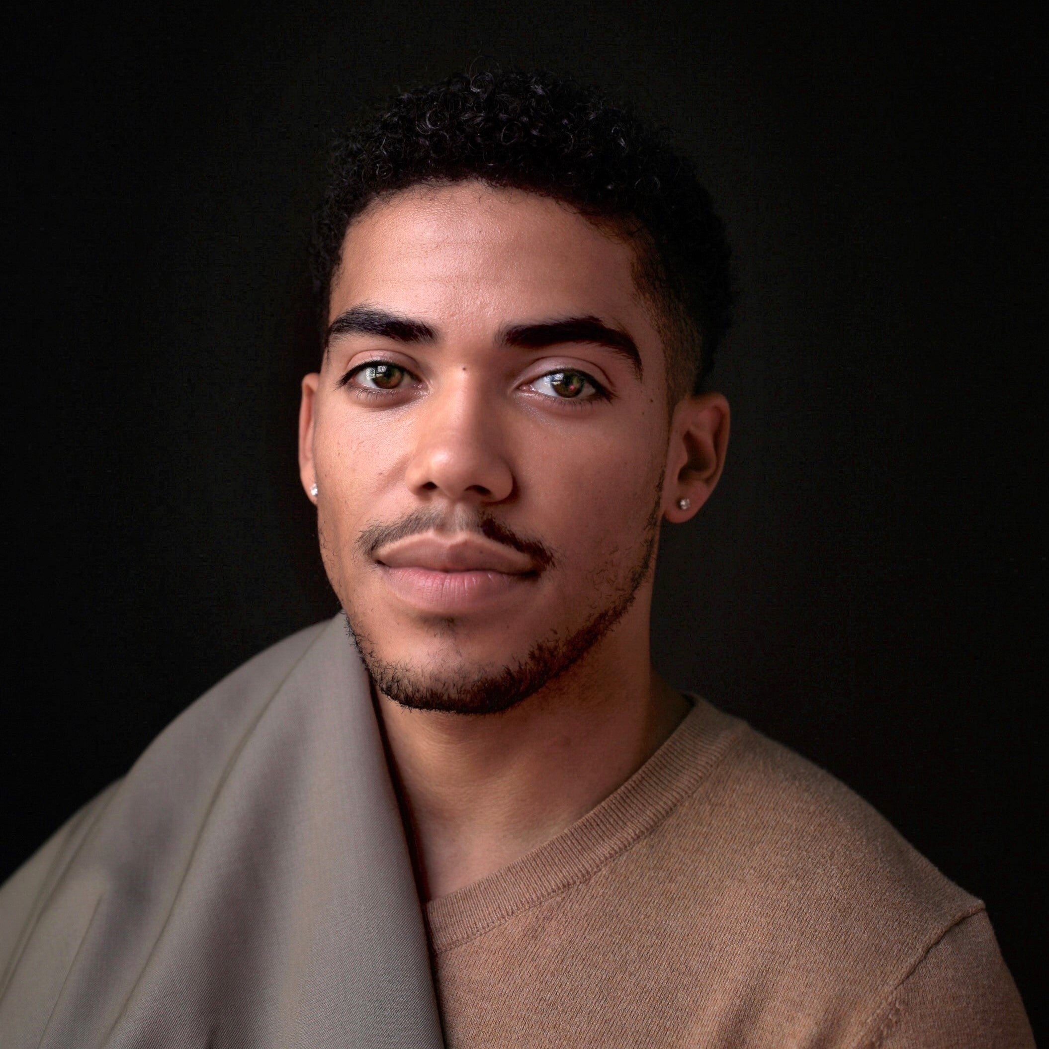 Racially Ambiguous Man wearing a brown sweater against a black background with a grey sheet on shoulder